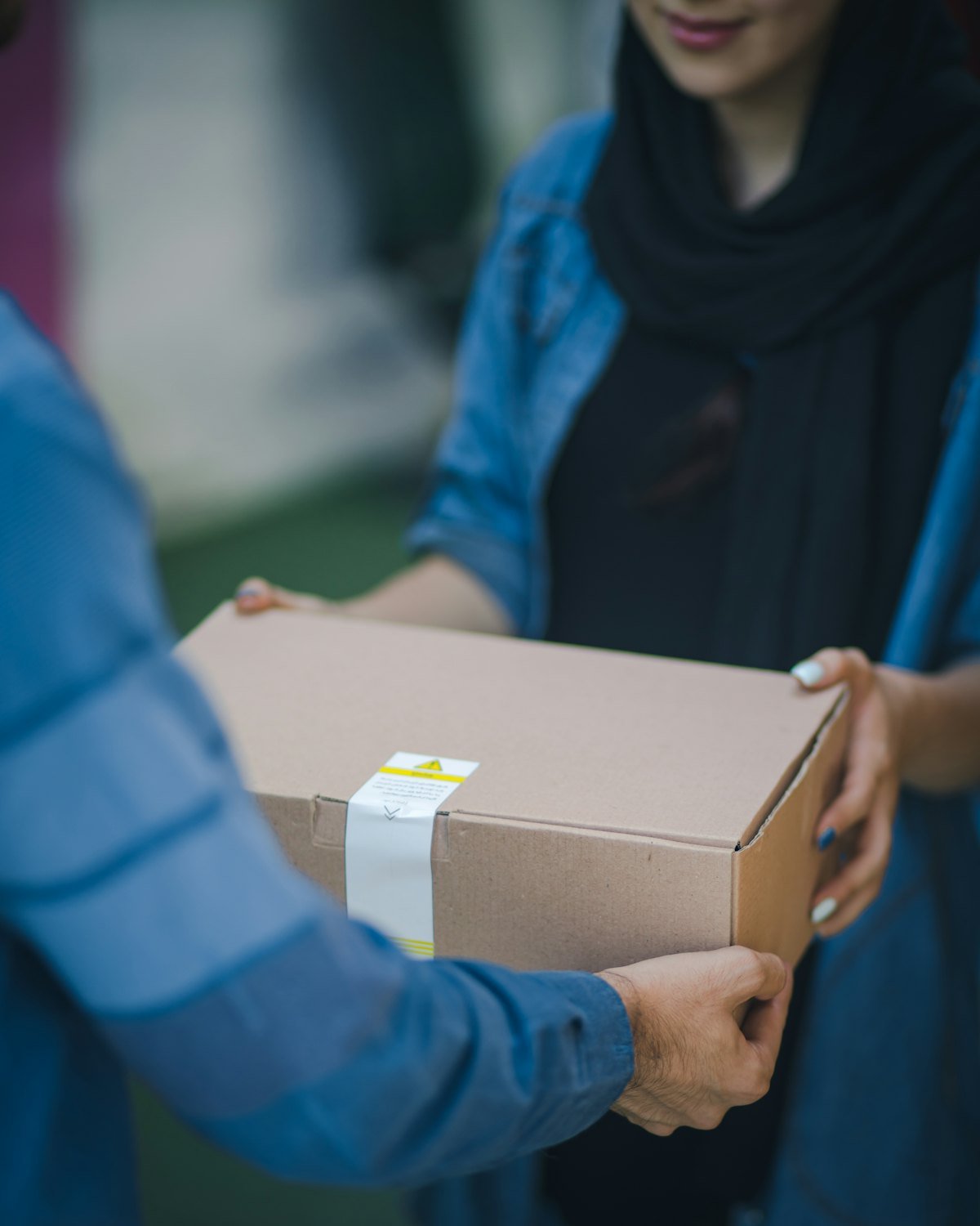 Two people holding a sealed brown cardboard box between them outdoors
